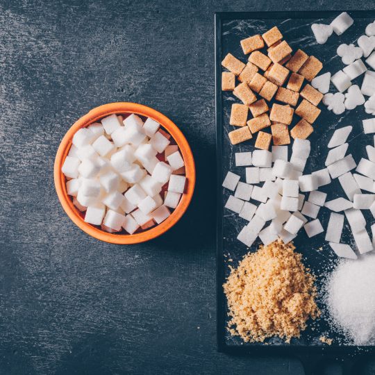 Brown and white sugar in a cutting board and bowl on a dark background. flat lay.